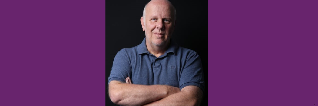 Professor Stephen Gorard standing with his arms crossed against a black background