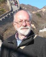 Photo of Bob Layton outdoors with a large winding wall and mountains in the distance behind him.