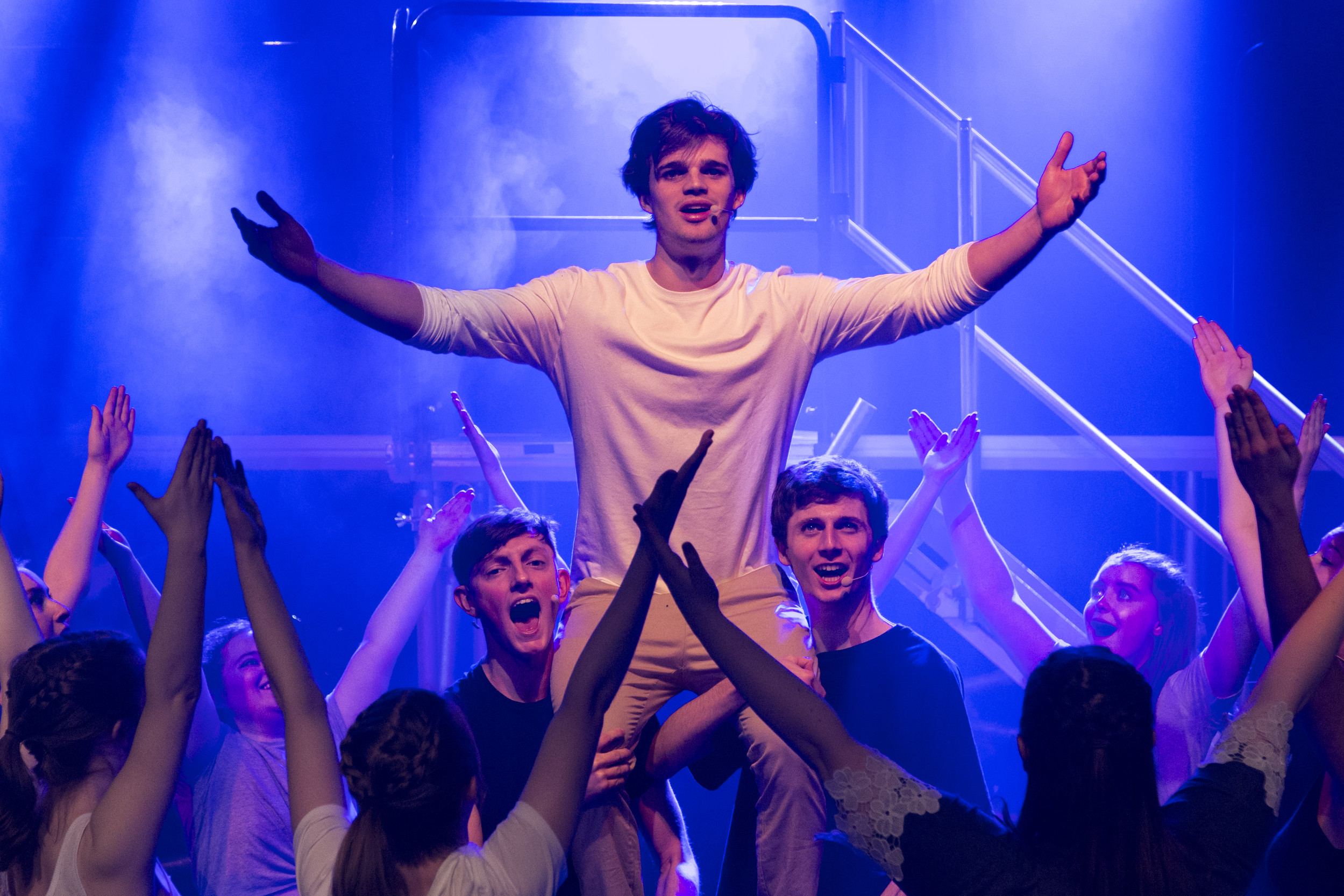 Musical theatre cast holding up lead actor