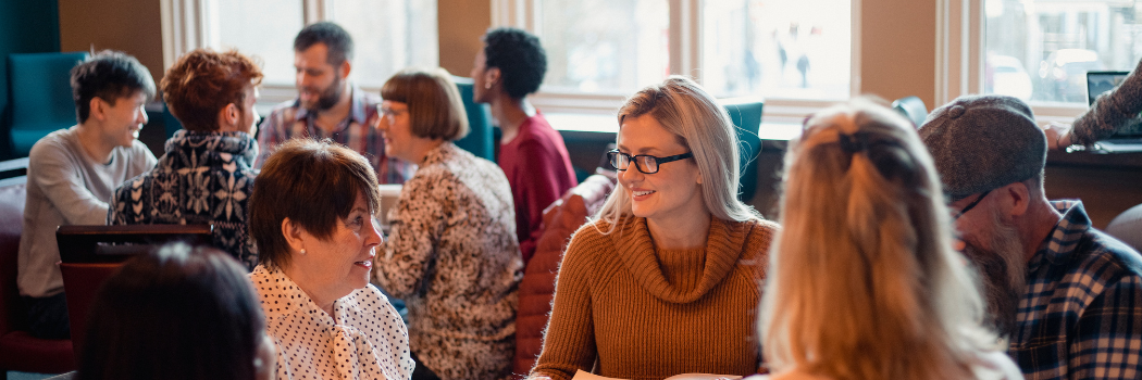 Small group of people with a mixed age range sitting around a table in a café