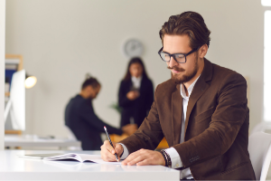 Academic man writing at desk with others in background