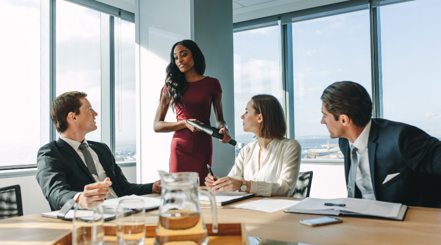 TA businesswoman stands and addresses three seated male colleagues at a table