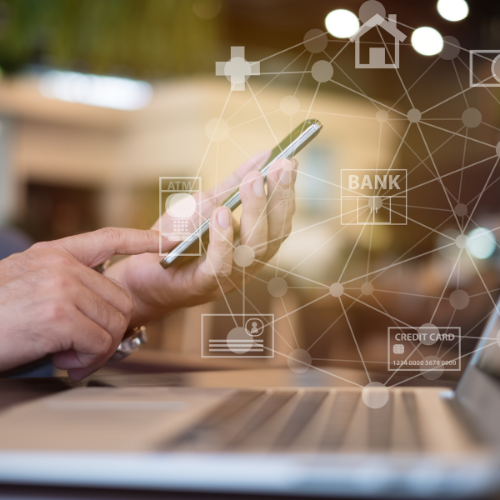 Man sat at a PC with mobile phone on online banking with floating banking icons