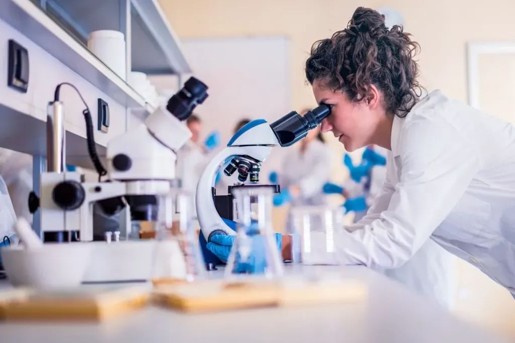 A woman scientist in a science lab looks into a microscope