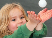 Child at Celebrate Science holding a ping pong ball above her hands