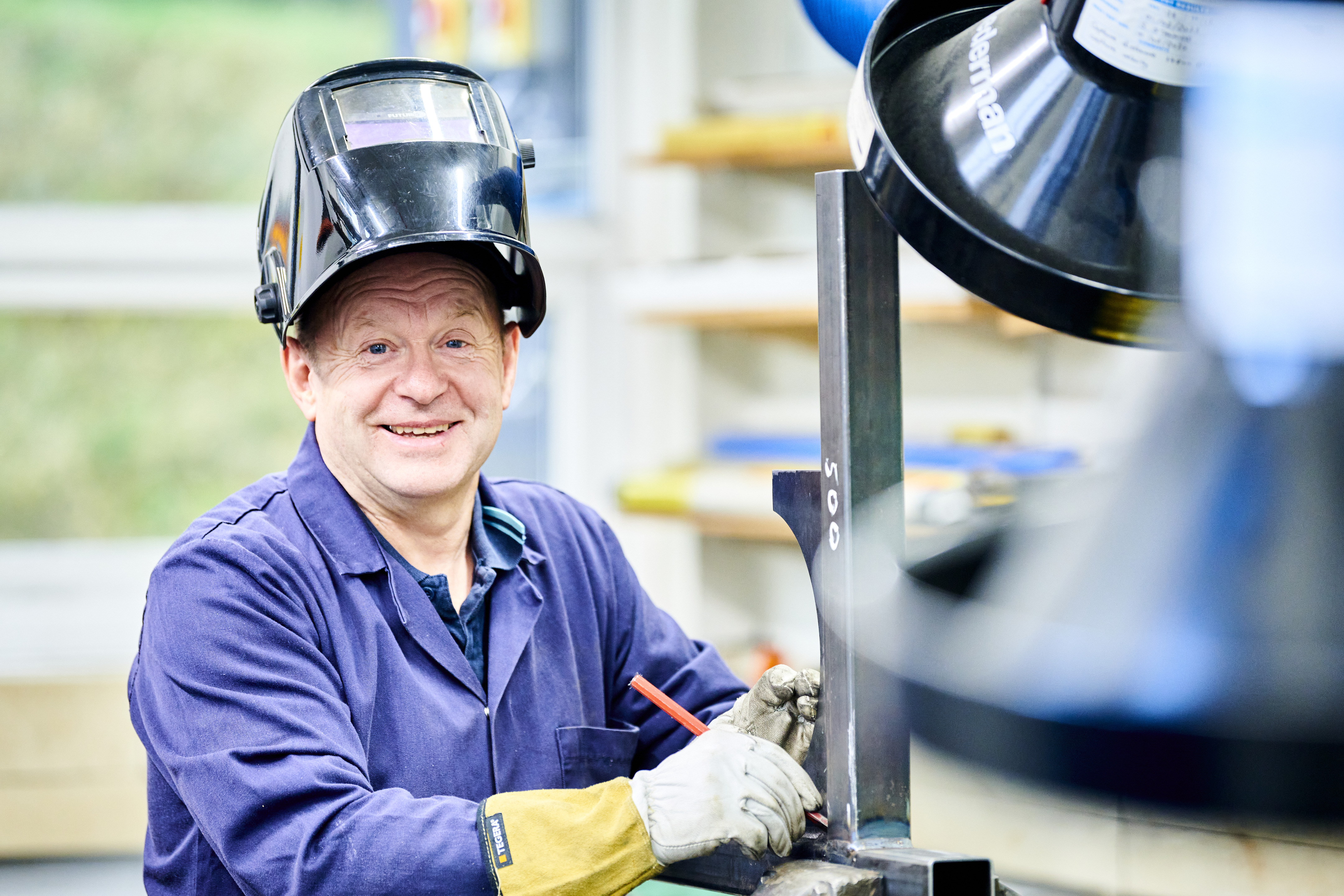 A smiling mature male student wearing safety gear works at an engineering machine