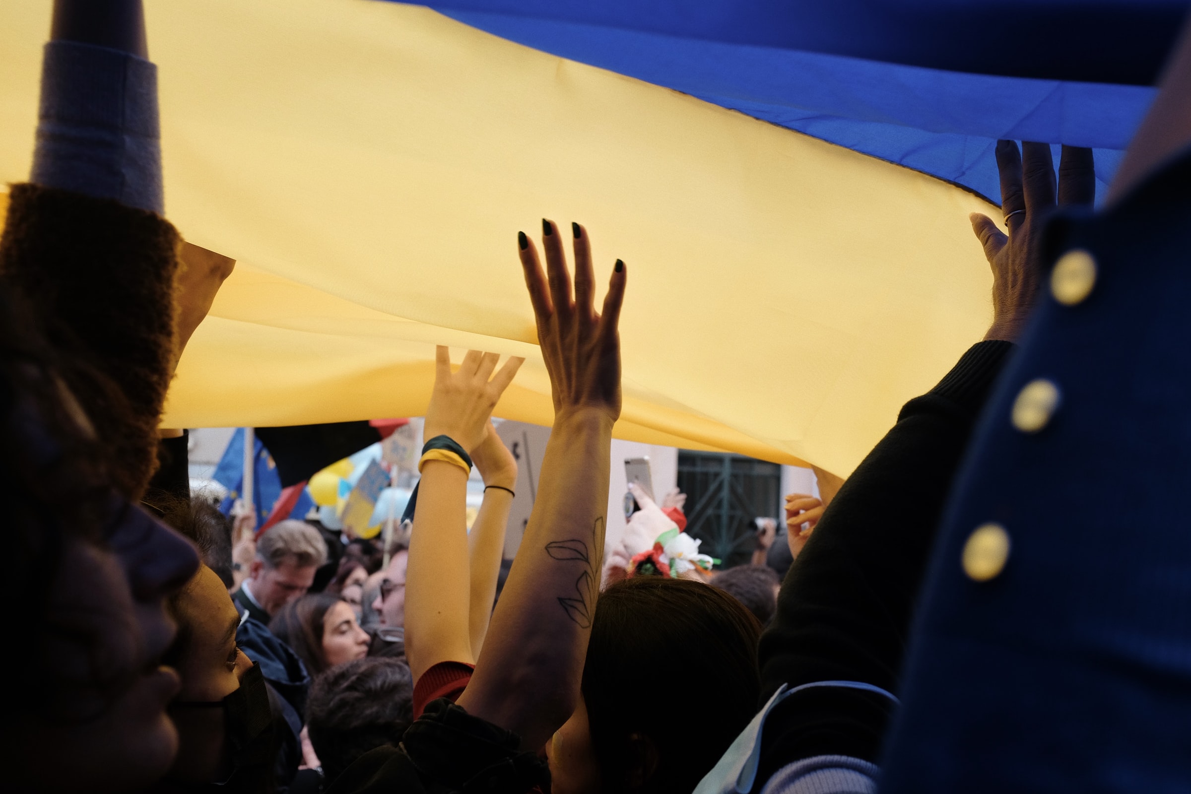 A crowd holding up a large Ukrainian flag during an anti-war protest