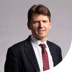 A photo of a man wearing a suit and a red tie looking at the camera.