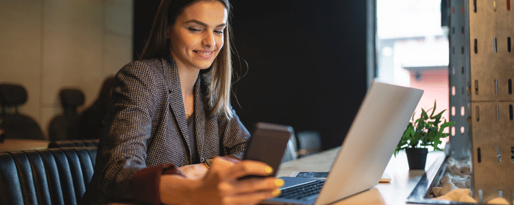 A woman looking at her phone in front of a laptop