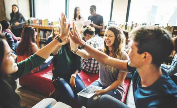 A group of students high fiving in the air while sat on sofas