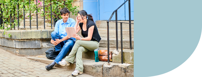 Two students sat on a step in front of a blue door in a city street