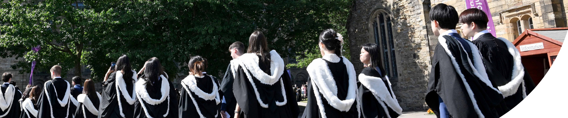 A large group of students in congregation gowns from behind walking on Palace Green