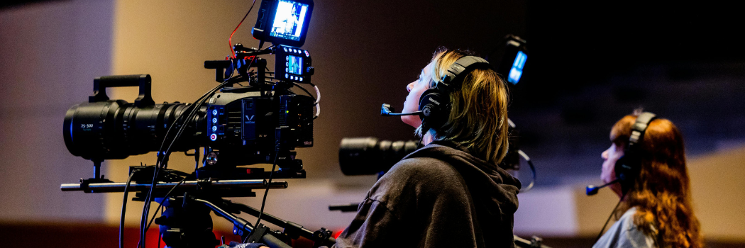 A camera operator looking into a professional broadcast camera screen while wearing headphone