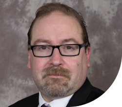 A man wearing black framed glasses and a suit looking at the camera