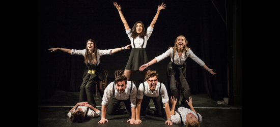 Students performing on stage in a pyramid with arms raised