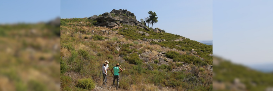 Three people standing on a hill next to a ruin.