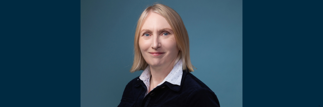 Professor Carol Adams facing the camera with a blue background behind her