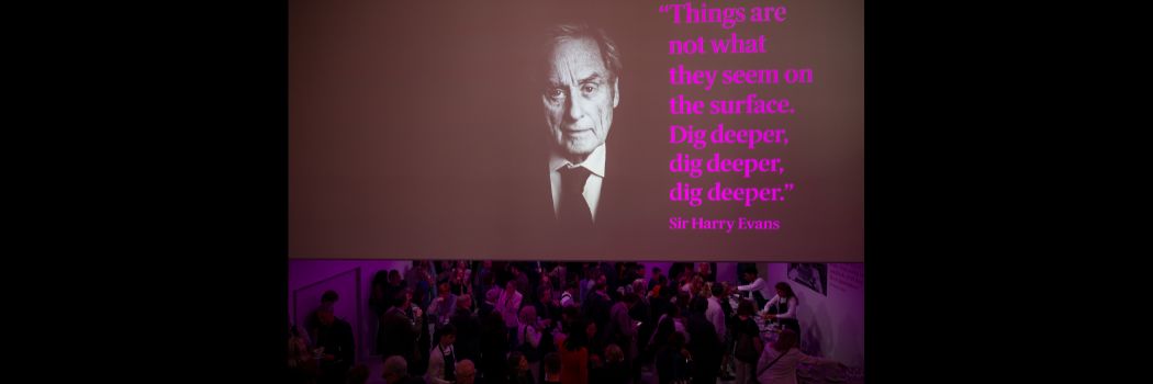 A black and white photo of an older man, with text to the right, hanging above a crowded room