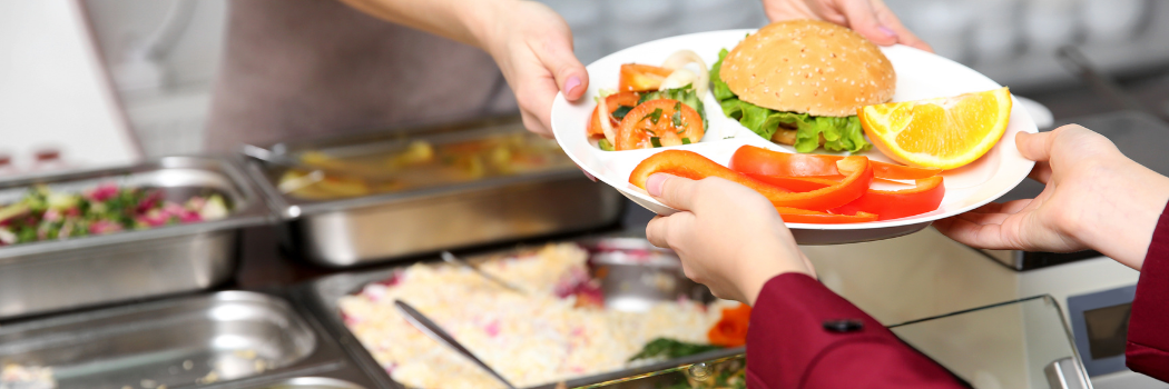 Someone handing a plate of food including a burger and salad to a customer