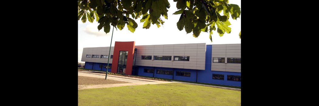 A wide shot of the exterior of a modern, factory-like building, with grass in front