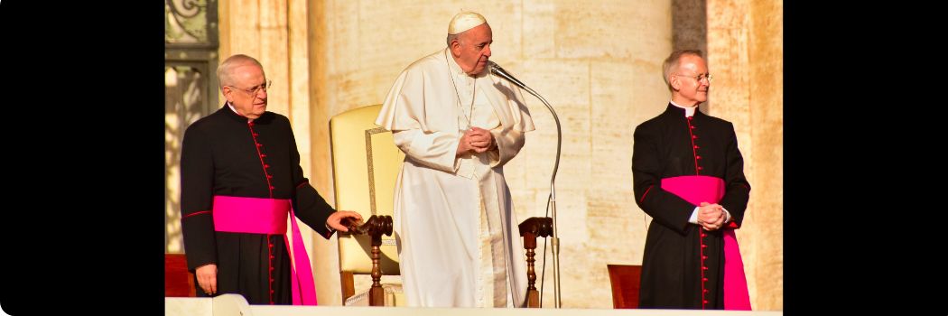 Pope standing at microphone with a cardinal standing on either side