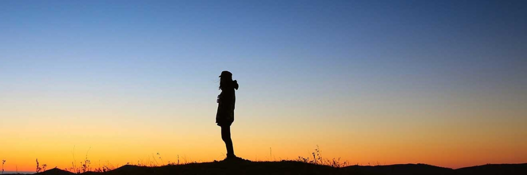 Sky at sunset with a lone person looking out away from the camera in silhouette