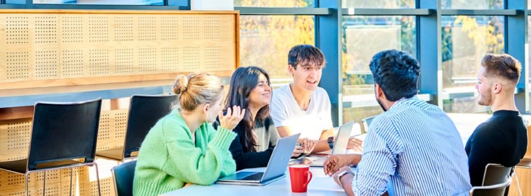 Group of students in discussion in boardroom with laptop