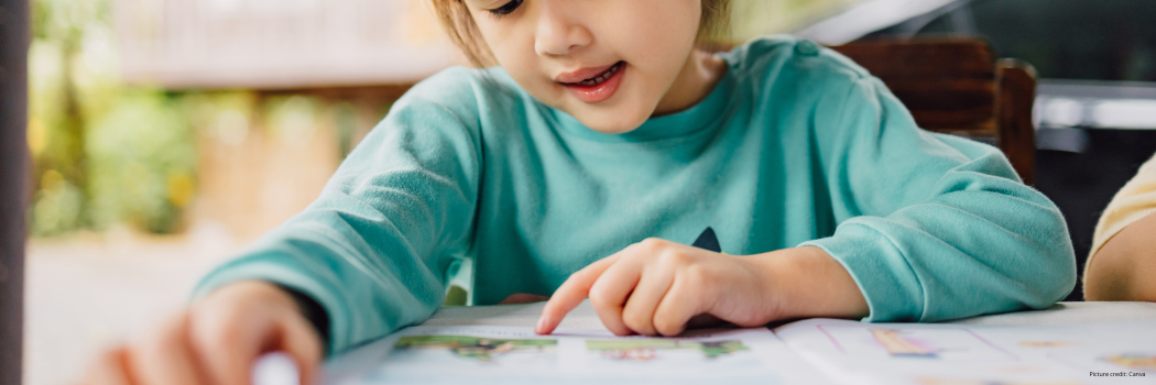 A young girl reading a book whilst following the words with her fingers on the page.