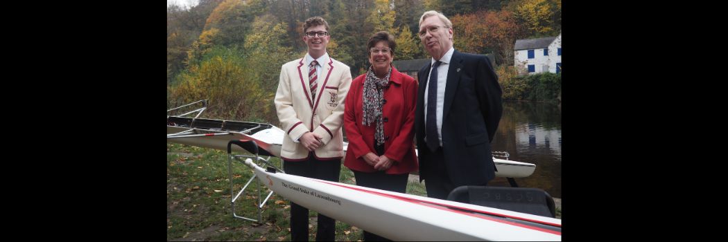 Three people standing behind a rowing boat, in front of a river