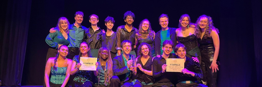 A mixed group of students all wearing at least one teal coloured item pose in two lines with two certificates on a stage.