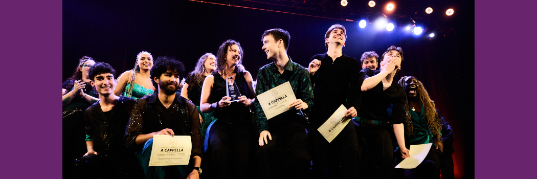 A mixed group of students on a stage holding four certificates and a glass trophy. All look very happy.
