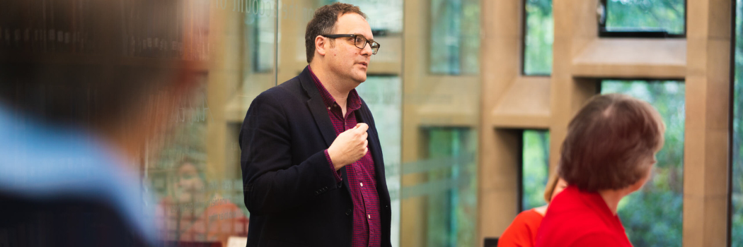 A man stands giving a speech in front of several people