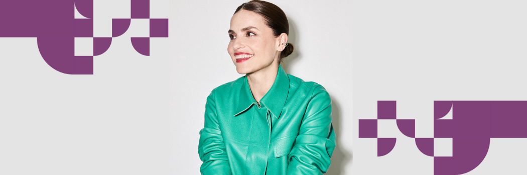 A dark haired woman in a green top smiles looking slightly off-camera