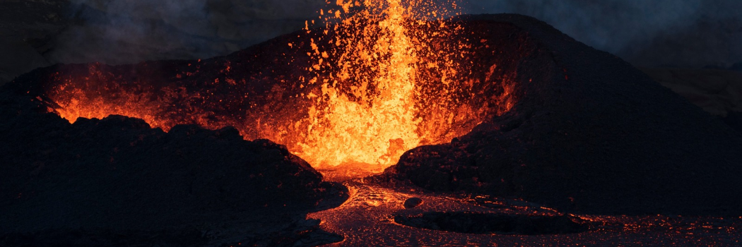 A volcano erupting bright orange fire with a lava flow underneath against a dark sky