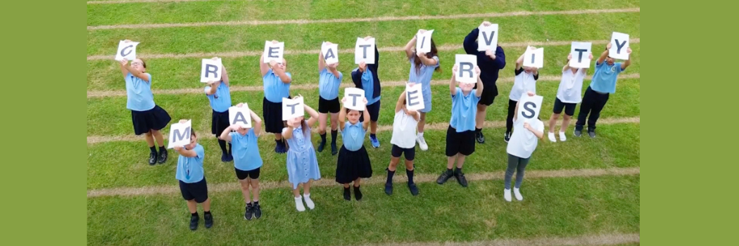A group of schoolchildren wearing blue uniforms standing on grass holding letters that read ''Creativity Matters'