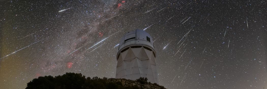 The dome of a telescope on top of a hill with a starry sky behind it.