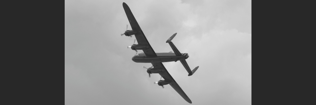 A Lancaster bomber plane flies over a cloudy gray sky