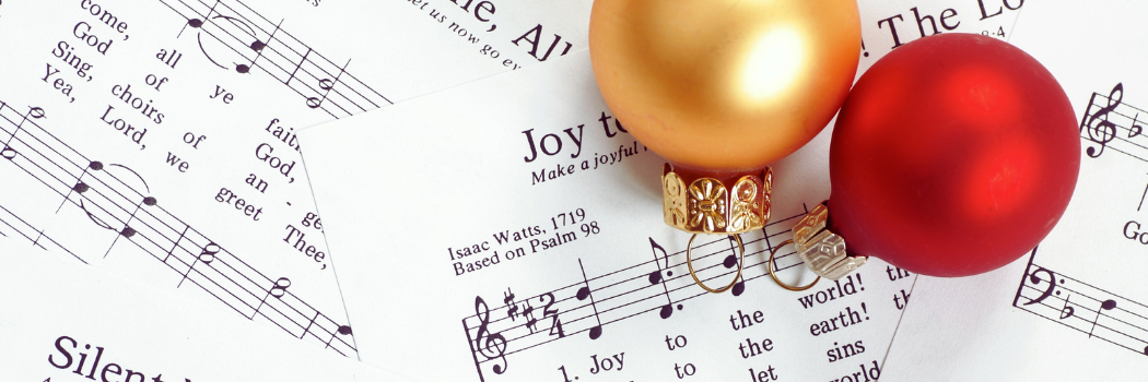 Christmas tree ornaments sitting on sheet music for Christmas carols