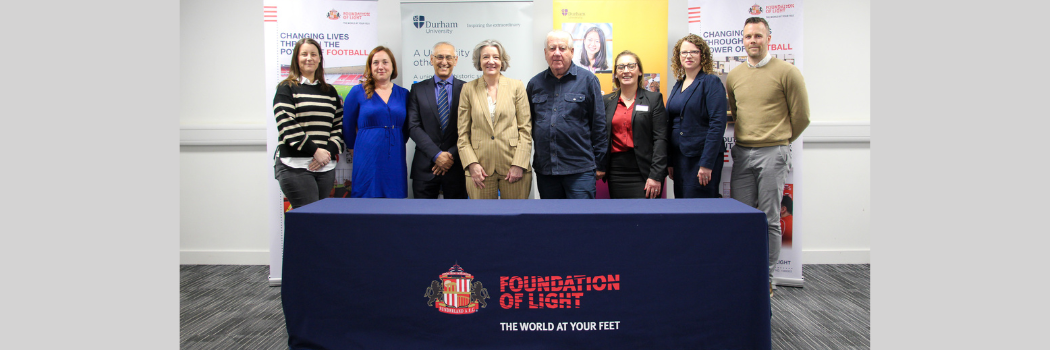 A group of university and charity representatives stood behind a table smiling