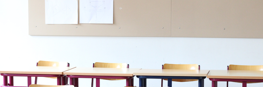 Empty classroom desks and chairs in front of a notice board