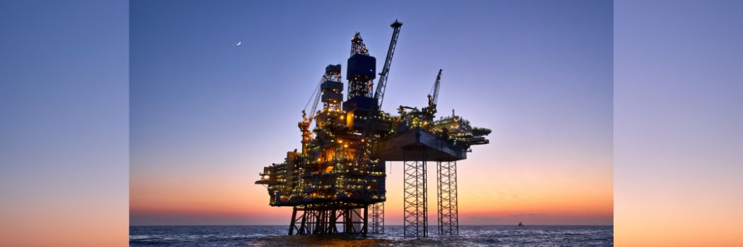 A photograph of an oil and gas rig in the North Sea, against a blue and yellow sky at dusk.