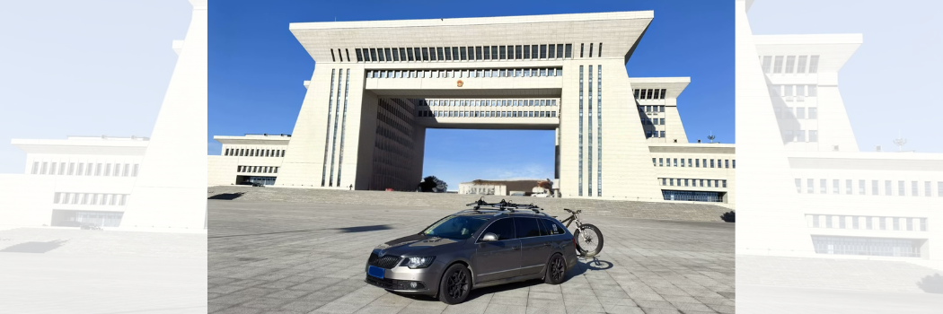 A car with a bike on the back in front of an imposing bridge-like building