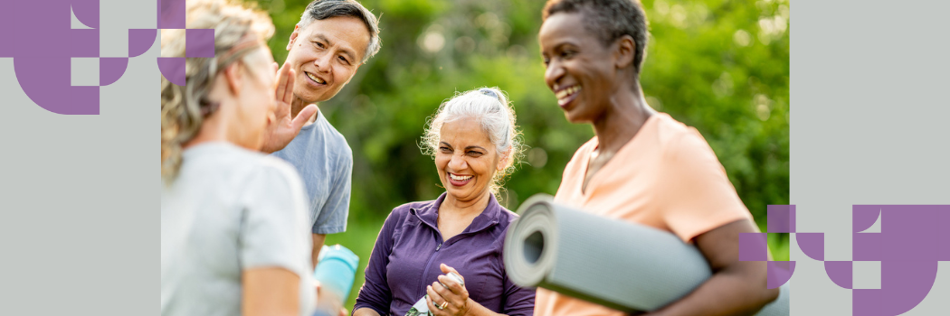 A group of four men and women in a park laughing with yoga mats rolled under their arms.