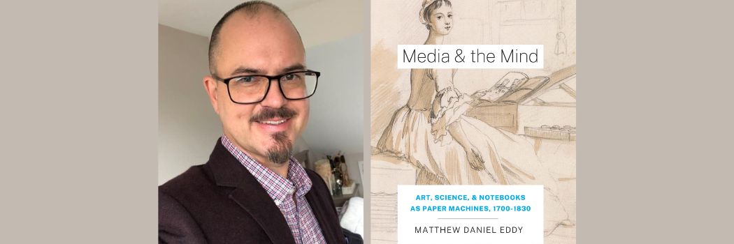 A man wearing glasses and smiling at the camera next to a book cover of a painting of woman in period dress. The book is called Media & Mind.