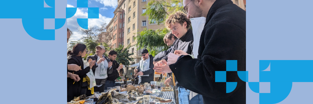 A group of young people in the sunshine outdoors standing at a table eating