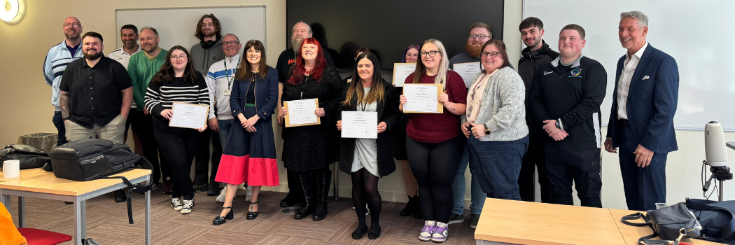 A group of men and women smiling at the camera, some holding up certificates.