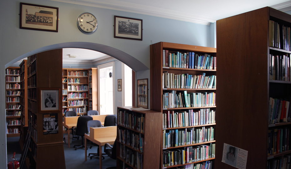 Library shelves with a view through an archway to the desks where students are reading.