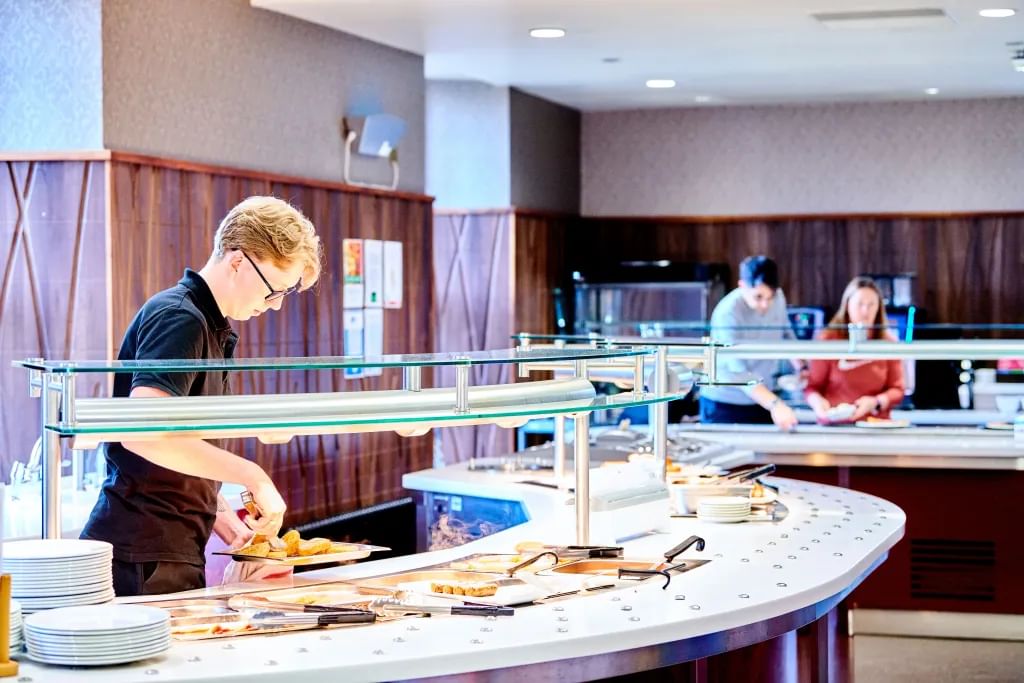 Male server staff plating up some hash browns at a white topped servery, in a wood-panelled room