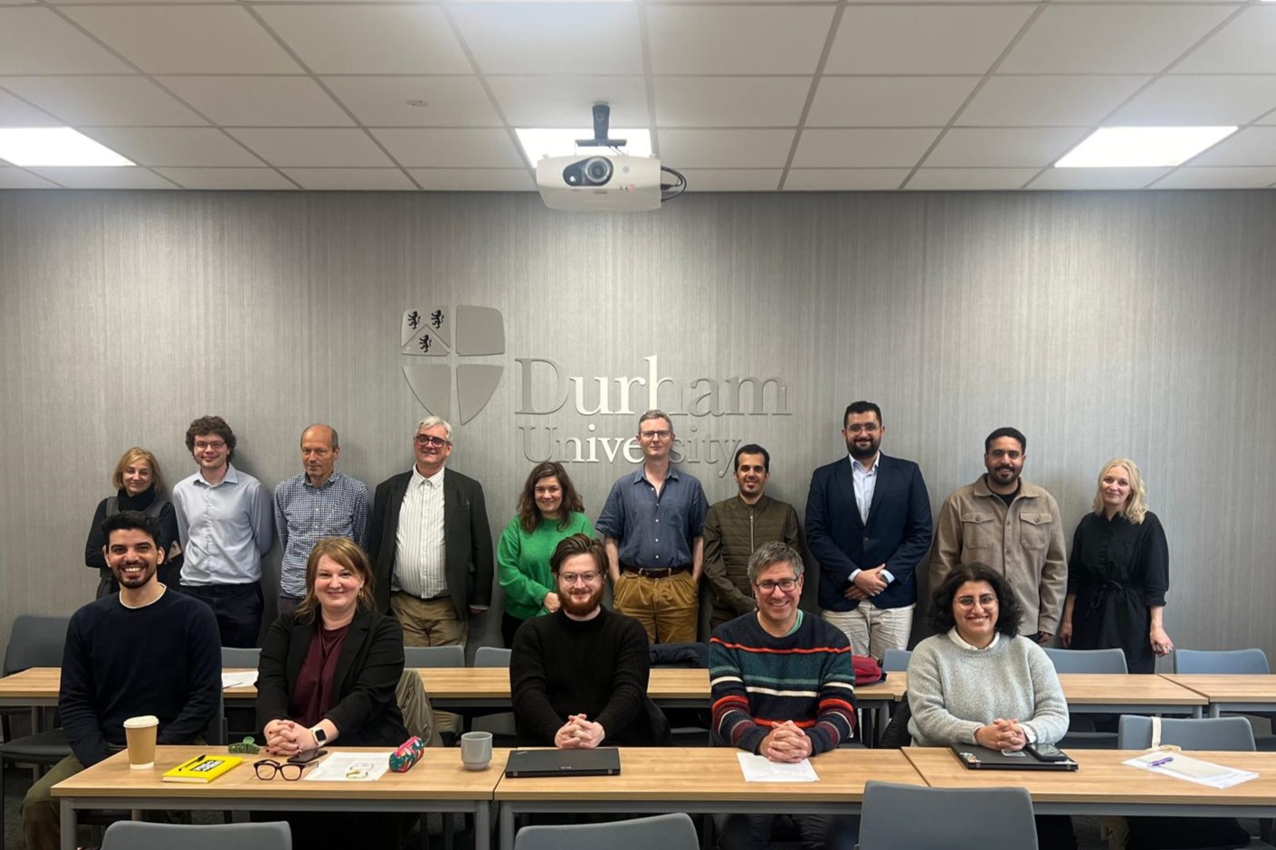 Group photo of 15 workshop attendees in the Department of Archaeology's Birley Room. On the back wall is the Durham University logo.