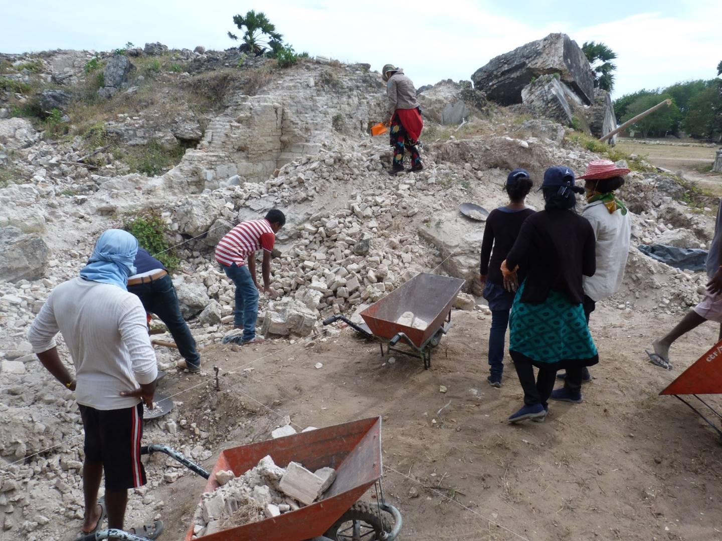 Photograph of archaeologists removing rubble to expose a wall